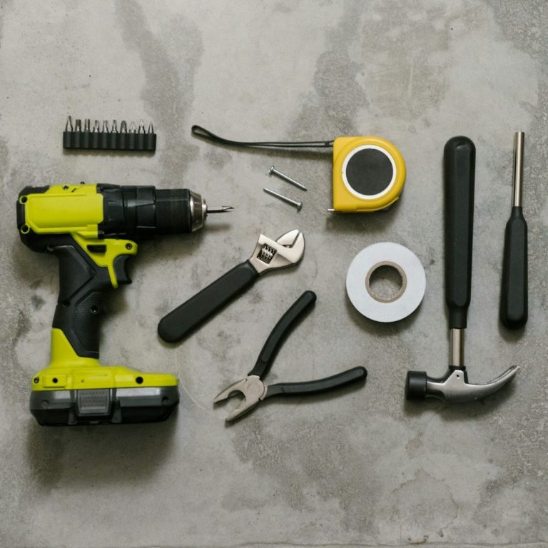 Tools arranged on a concrete surface: drill, pliers, tape measure, hammer, and screws.