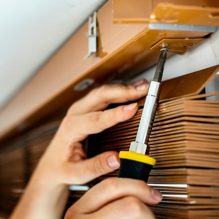 Hand using a screwdriver to adjust a window blind mechanism.